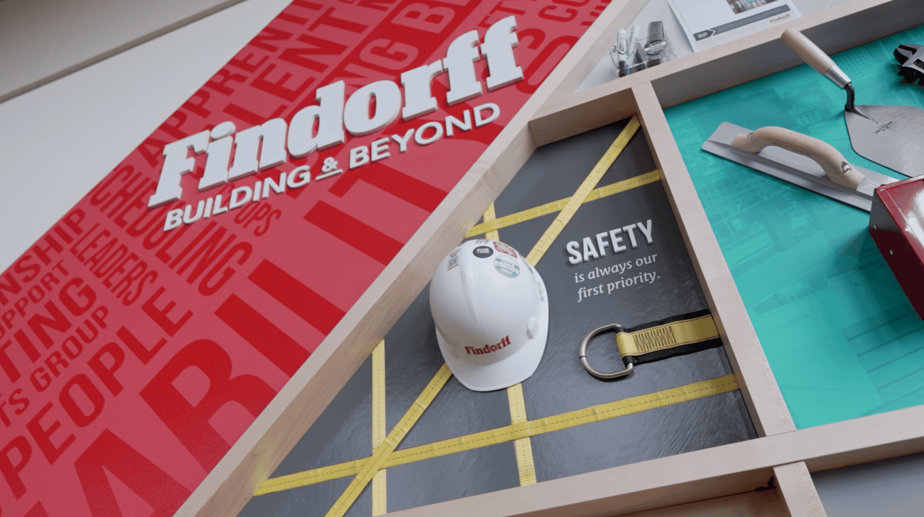 Findorff facility branding display by Thysse featuring a hard hat with safety messaging, emphasizing 'Safety is always our first priority,' alongside tools and equipment against a branded, visually engaging backdrop.